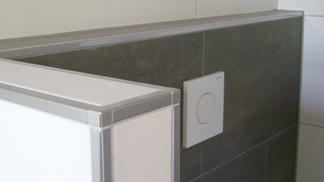 Detail van het tegelwerk in de wc. Langs de witte tegels is een bies met chromen tegels voor extra luxe effect